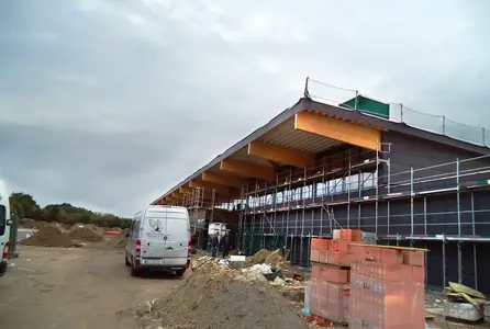 Elektrotechnik im Einzelhandel bei einem Verkaufsgebäude im Rohbau mit Gerüst, Baustellenfahrzeug und Baumaterial.